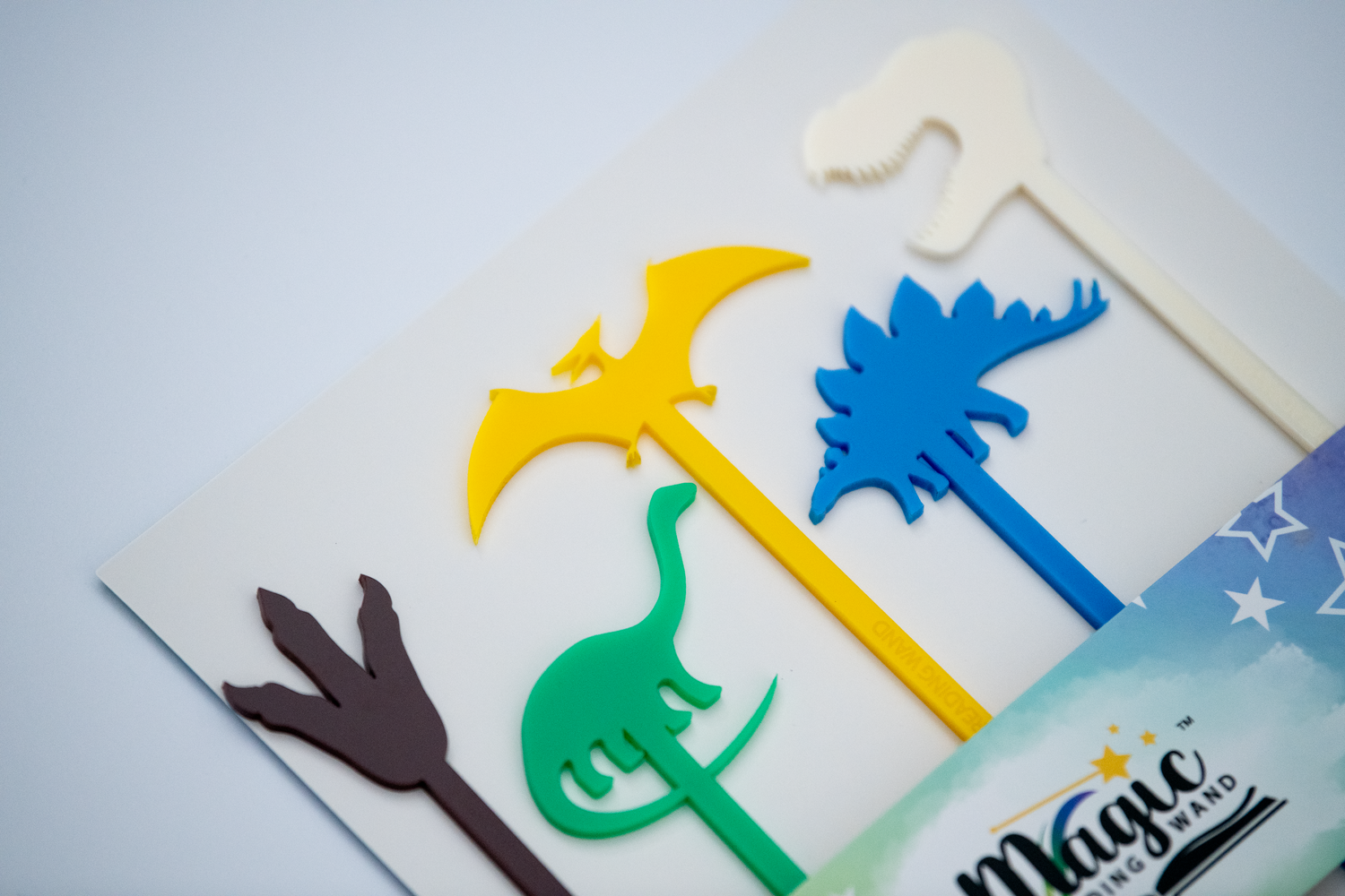 Colorful dinosaur-shaped cake toppers on a white surface with 'Magic Reading Wand' branding.